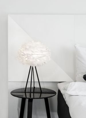 Eos Mini lampe fra Umage i hvit. Plassert på en bordlampe ved siden av en seng, lys på