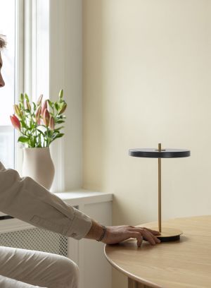 Asteria Move oppladbar bordlampe på et bord med noen som trykker på bryter. Foto. 
