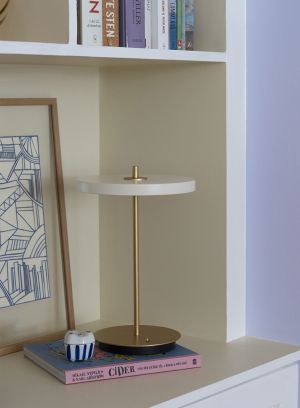 Asteria Move opplad bordlampe fra Umage i hvit. Står på en skjenk sammen med bøker og maleri. lys av