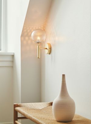 Miira vegglampe - gull/klart glass i et hjørnet i en stue