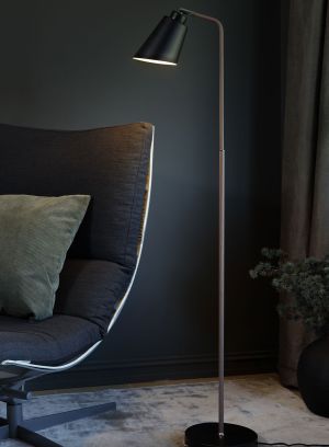 København gulvlampe i tre fra Høvik lys med svart skjerm plassert ved en stol, lys på