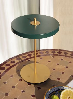 Asteria Move oppladbar bordlampe fra Umage i mørkegrønn. Plassert oppå et rundt bord som er plassert ute. lys av