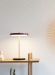 Asteria Move oppladbar bordlampe fra Umage i rubinrød. Plassert oppå et sidebord av lyst tre. lys på