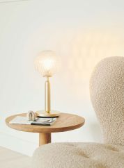 Miira bordlampe gull/optisk glass på et sofabord med lyset tent. 