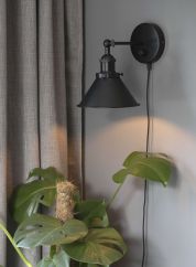 Anton vegglampe sort som lyser opp en plante i stuen. 