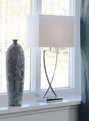 Omega bordlampe H69 fra By Rydens i sølvfarge med hvit skjerm. Plassert på en vinduskarm ved siden av en grå vase. lys på