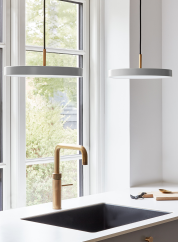 Asteria mini taklampe fra Umage i lys grå. Henger to stykker sammen over en kjøkkenvask og foran et vindu. lys på