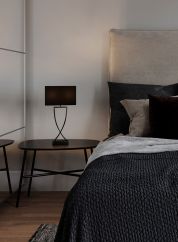 Omega bordlampe H52 fra By Rydens i sort. Plassert på et sort bord ved siden av en seng, lys på