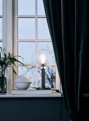 Miira bordlampe grå/optisk i vinduskarm med lyset tent. 