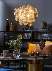 Gross taklampe fra By Rydens i gullfarget glass. henger over sort stuebord med sofa ved siden av. lys på
