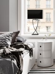 Omega bordlampe H69 fra By Rydens i sort. plassert på en vinduskarm bak en hvit seng og nattbord. lys av