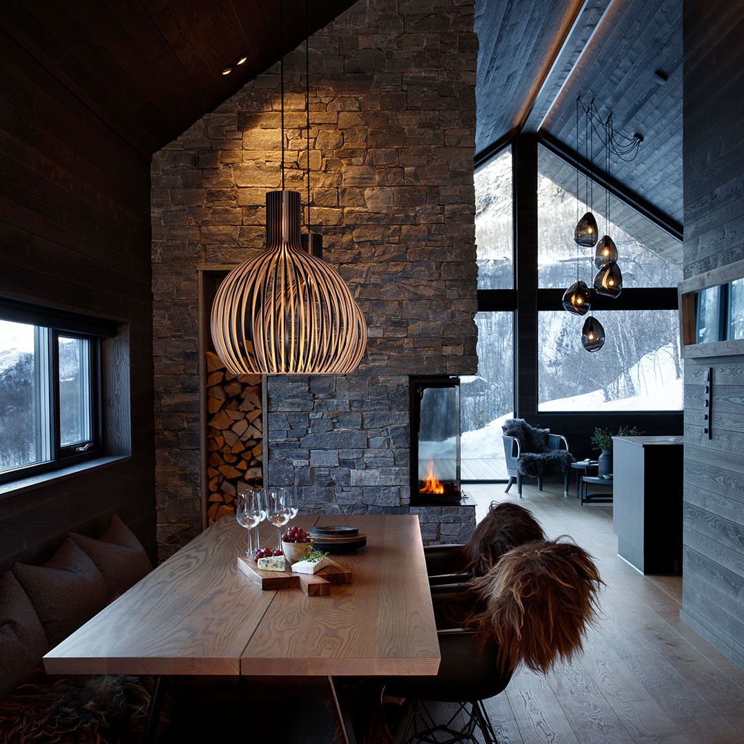En spisestue og stue på en hytte på fjellet med lamper over spisebord og salongbord